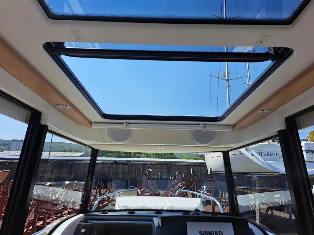 Interior view of a boat with a panoramic skylight, showing clear blue sky and nearby moored boats. Visible SIMRAD equipment.